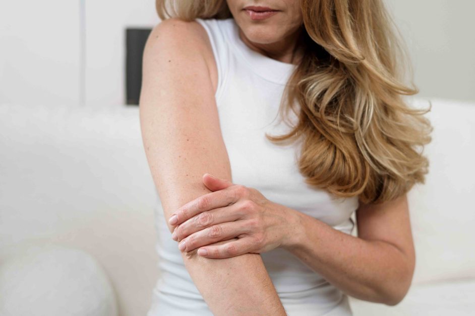 Pain in the elbow joint. Woman massage her arm. A mature female sits at home, gently scratching her arm due to eczema. Irritation suggest discomfort from chronic skin condition and stress on health