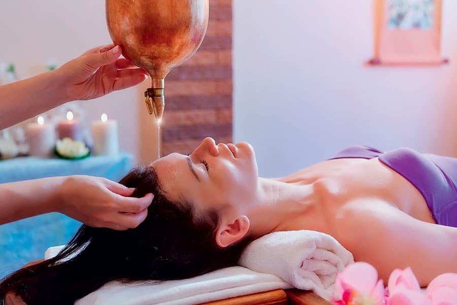 Jeune femme allongée sur une table de massage recevant de l'huile chaude sur le front.