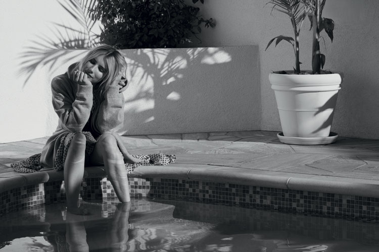 Emma Roberts posant pour un shooting au bord d'une piscine, les pieds dans l'eau.