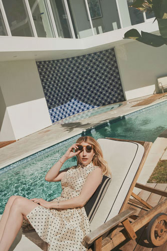 Emma Roberts posant pour un shooting, en robe, allongée sur un transat au bord d'une piscine.