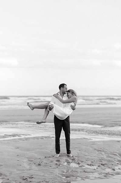 Jeune couple de mariés, l'homme portant la femme, sur une plage.