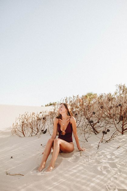 Jeune femme souriante en maillot assise sur une dune de sable.