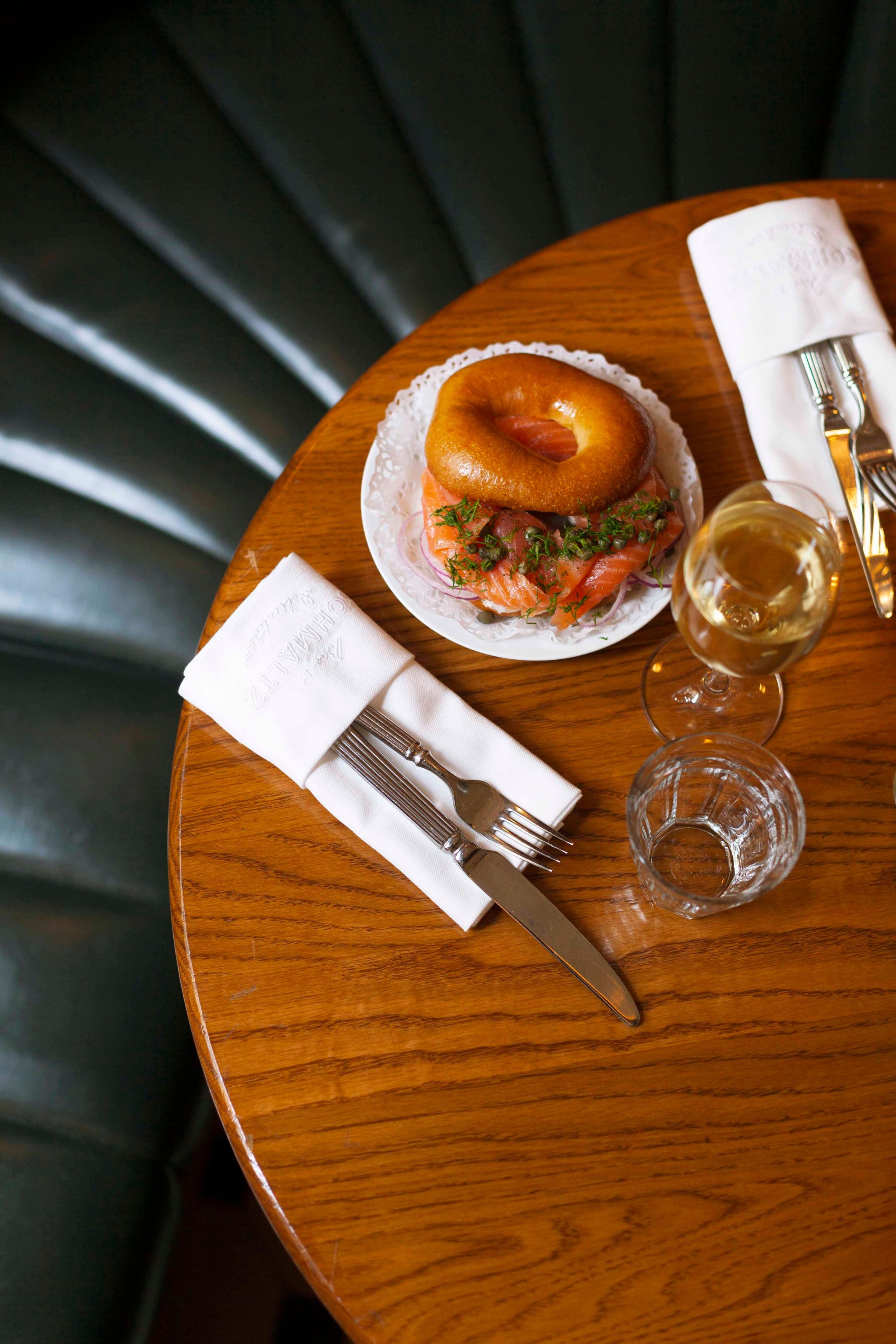 bagel sandwich with salmon on a wooden table with napkin and silverware.