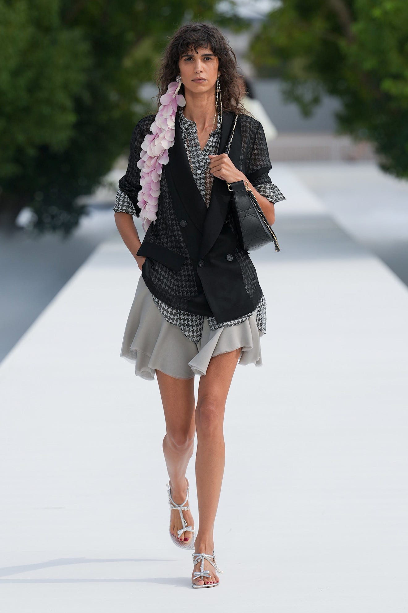 Model walking the runway in a stylish black outfit with floral accents and a gray skirt, showcasing modern fashion.