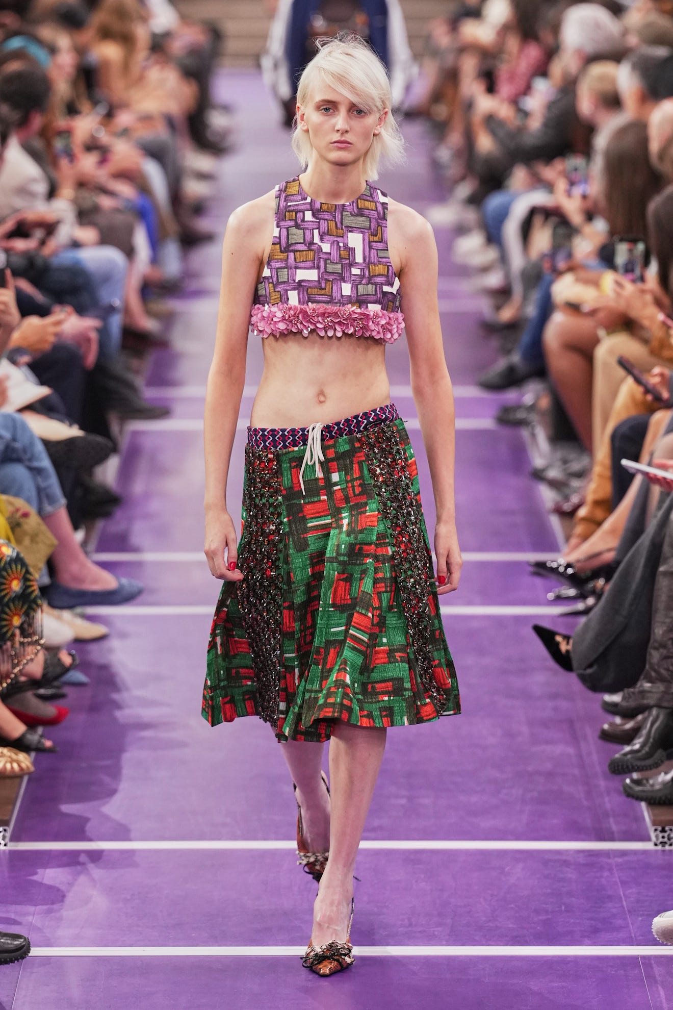 Model walking down the runway, wearing a colorful crop top and a full skirt, showcasing a vibrant fashion design.