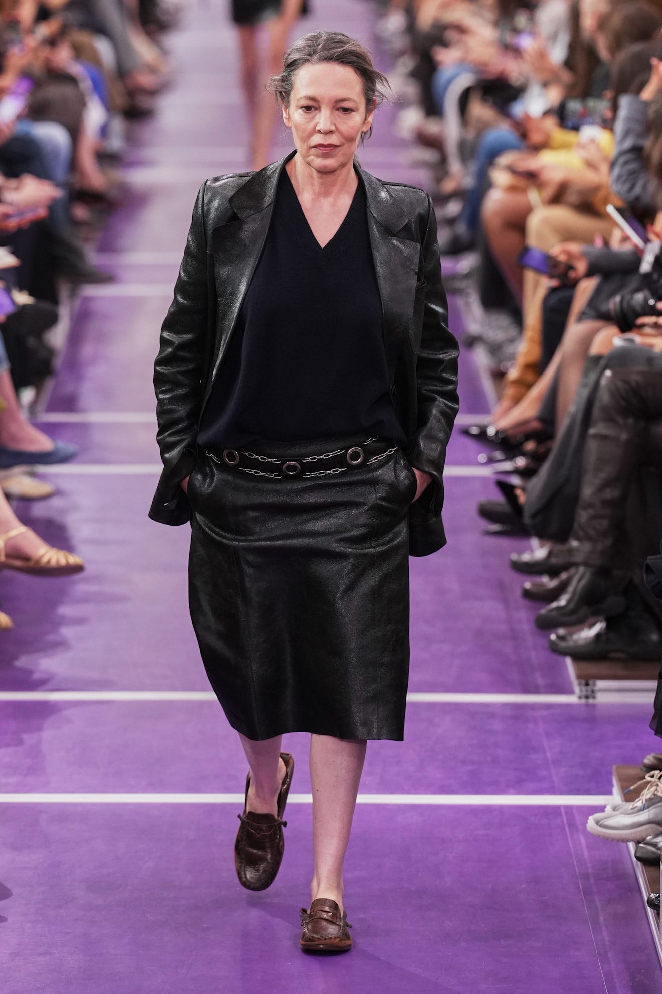 Model walking down the runway in a black leather outfit during a fashion show.