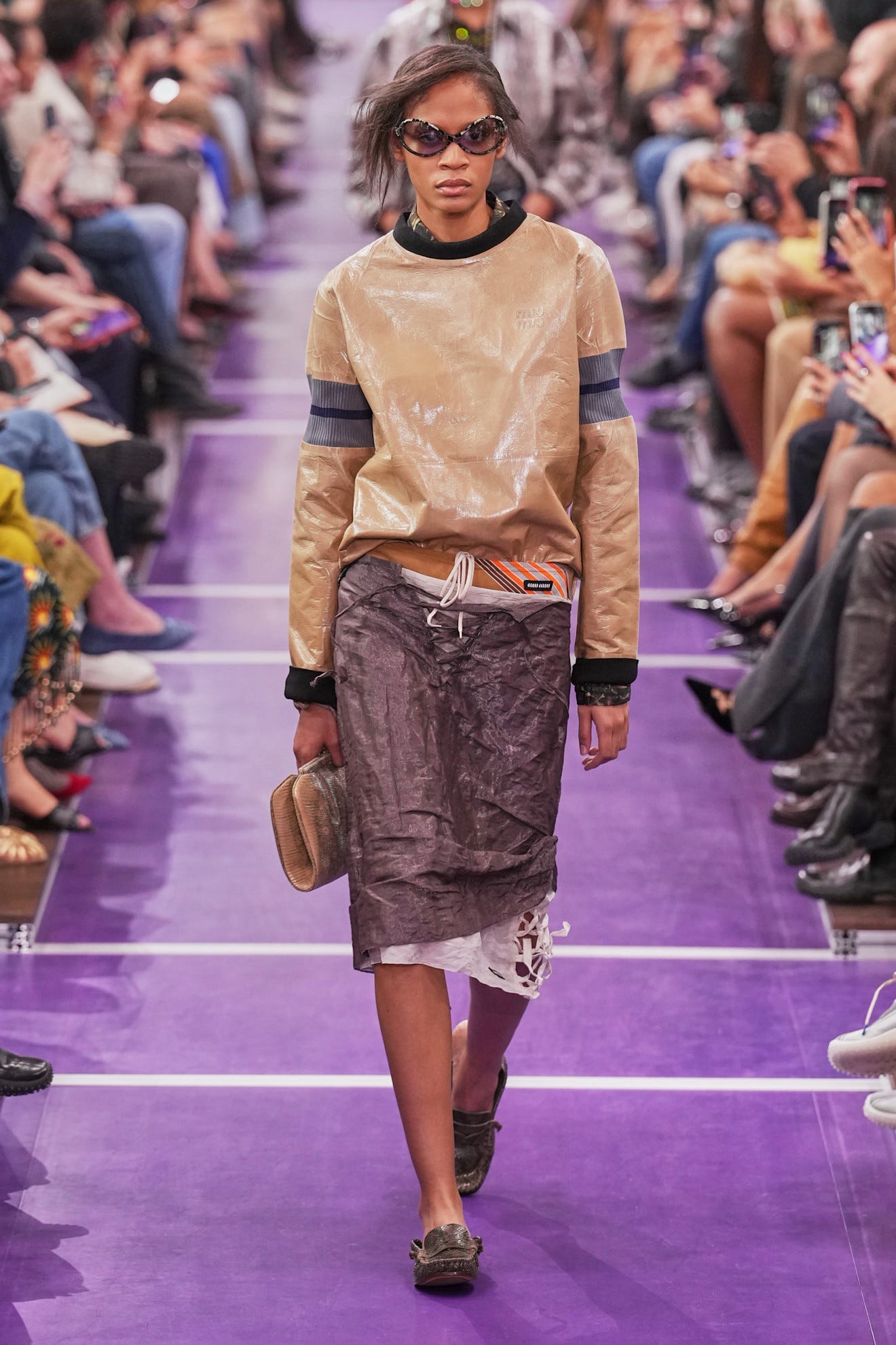 Model walking the runway in a unique outfit with oversized sunglasses during a fashion show.