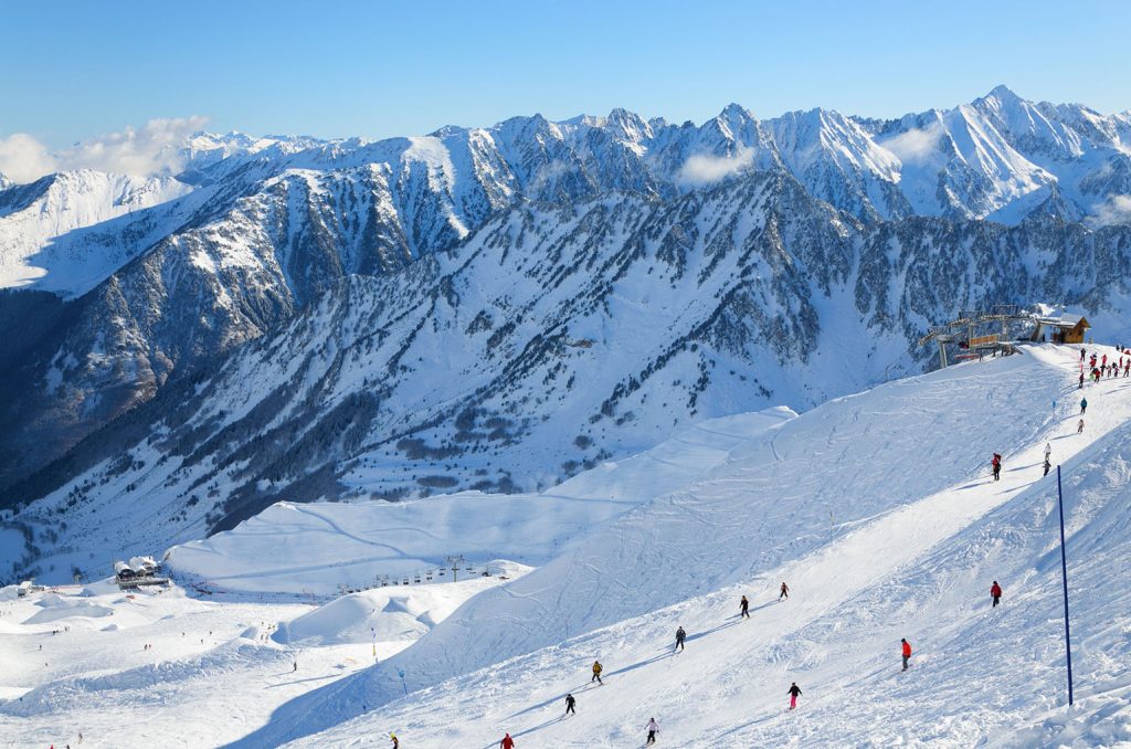 Skiers are sliding down snow-covered hill on skis at the Cirque du Lys. There is range of mountains (Soum de Mauloc) in the background. Winter Pyrenees is photographed at the Cauterets ski resort.
