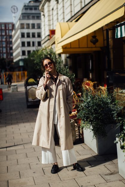 vrouw met flare jeans en trenchcoat